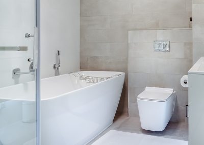 Bathroom with tiled walls and floors facing a toilet, shower and freestanding bath tub.